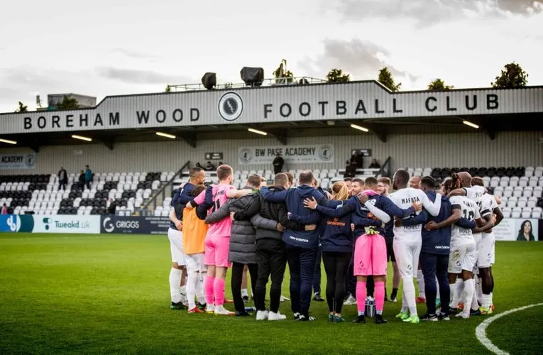 Đội hình Boreham Wood FC đứng trước khán đài chính của sân Meadow Park