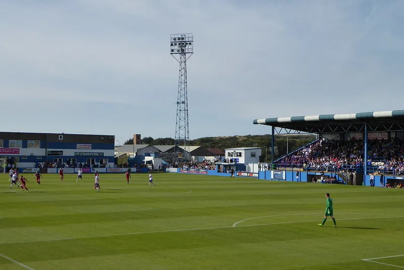 Một trận đấu bóng đá đang diễn ra trên sân Holker Street, sân nhà của đội bóng Barrow AFC